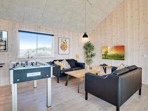 A modern living room with a foosball table, a sofa, a coffee table, and a television.