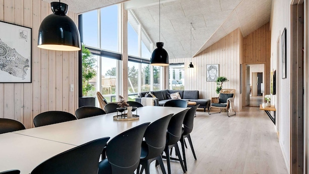 A modern interior with a long dining table, black chairs, pendant lights, and wooden paneling. - 5 Star Holiday Home in Ringkobing (Ringkobing)