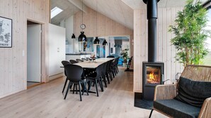 A modern interior with a dining area, a black stove, and a wicker chair. - 5 Star Holiday Home in Ringkobing (Ringkobing)