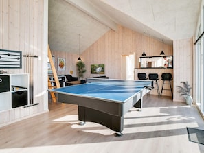A room with a ping pong table, a sofa, a TV, and a bar area with stools.