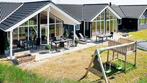 A modern building with large glass windows, outdoor seating, and a swing set. - 5 Star Holiday Home in Ringkobing (Ringkobing)