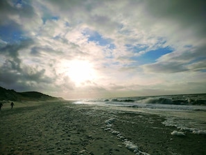 A beach with waves, a cloudy sky, and a person walking.