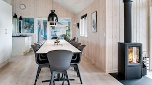 A modern kitchen with a dining area, wooden walls, a black stove, and a clock. - 5 Star Holiday Home in Ringkobing (Ringkobing)