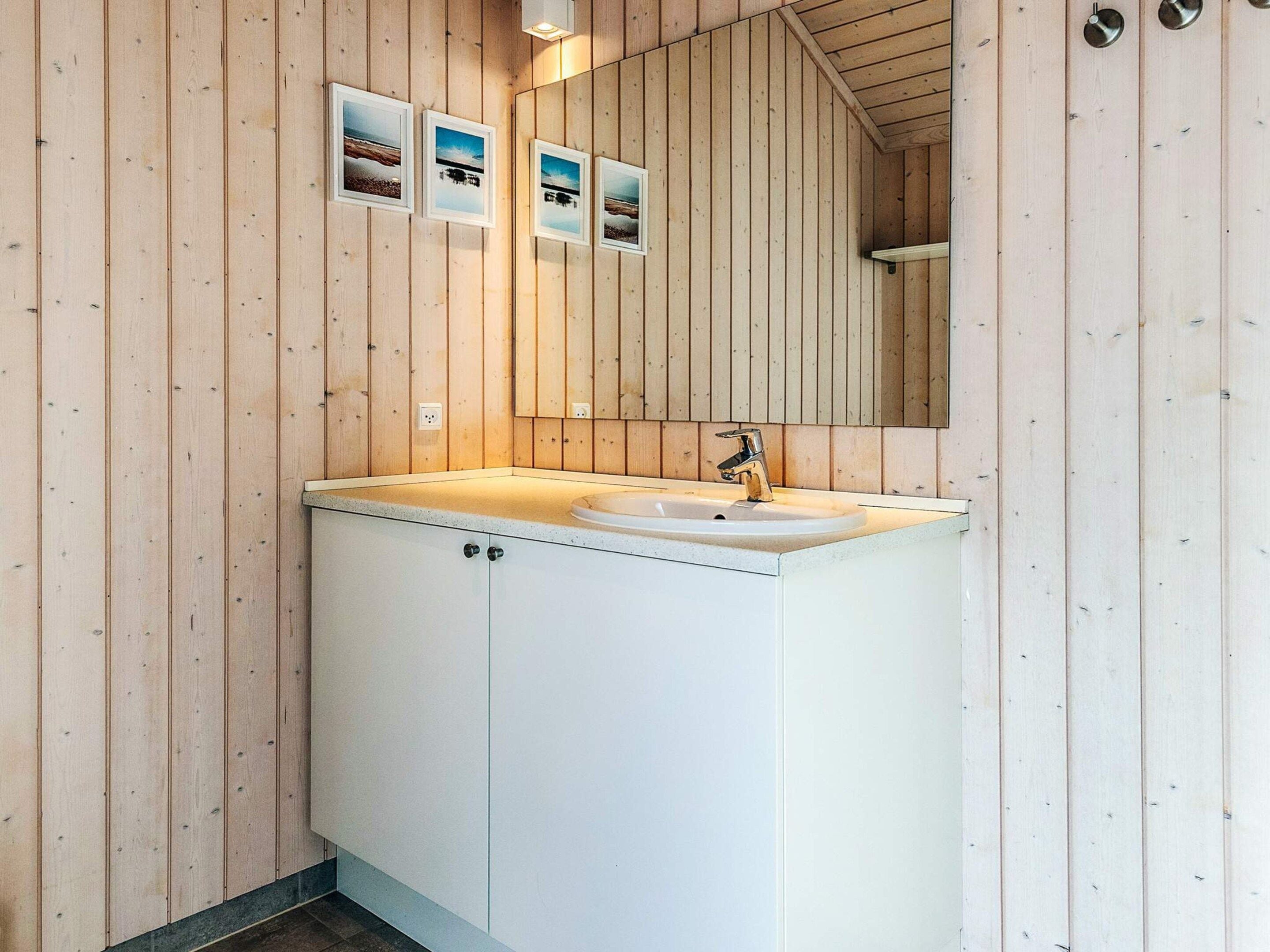 A modern bathroom with wooden panel walls, a white sink, and a mirror above it.