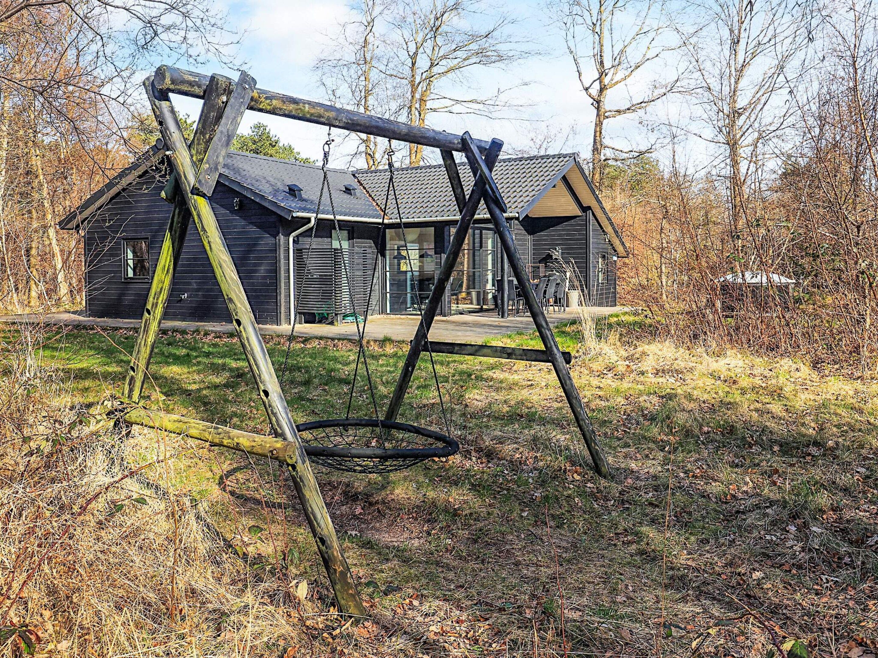A wooden swing set in a grassy area with a house in the background.