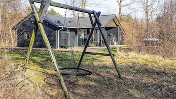 A wooden swing set in a grassy area with a house in the background.