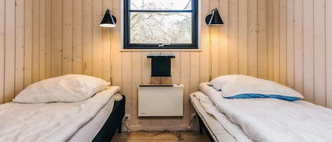 Una habitación pequeña y acogedora con dos camas individuales, una ventana que da a árboles y un escritorio pequeño con una lámpara.