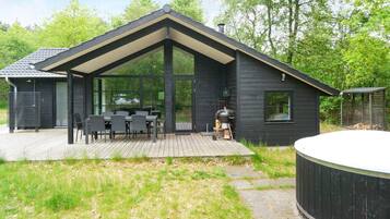 A modern house with a deck, a barbecue, and a hot tub.