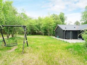 A grassy yard with a swing set and a small black building with a tiled roof. - 5 Star Holiday Home in Vig (Vig)