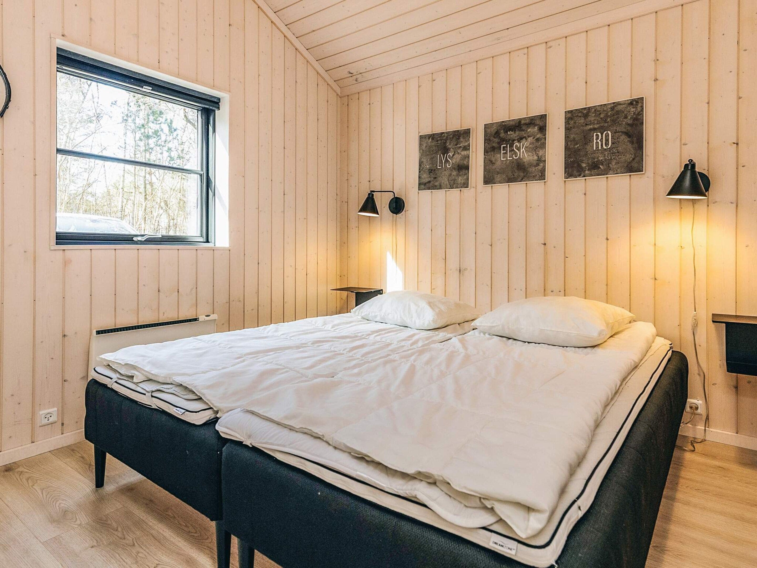 Makuuhuone, jossa on sänky, kaksi yöpöytää, ikkuna ja seinään kiinnitetyt valaisimet.