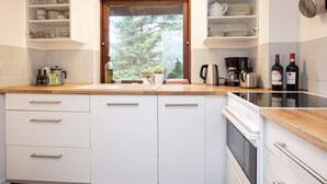 Una cocina con armarios blancos, encimera de madera, ventana con vistas a árboles y una estufa.