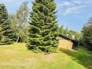 A single-story brick building with a sloped roof, surrounded by a grassy yard and several evergreen trees.