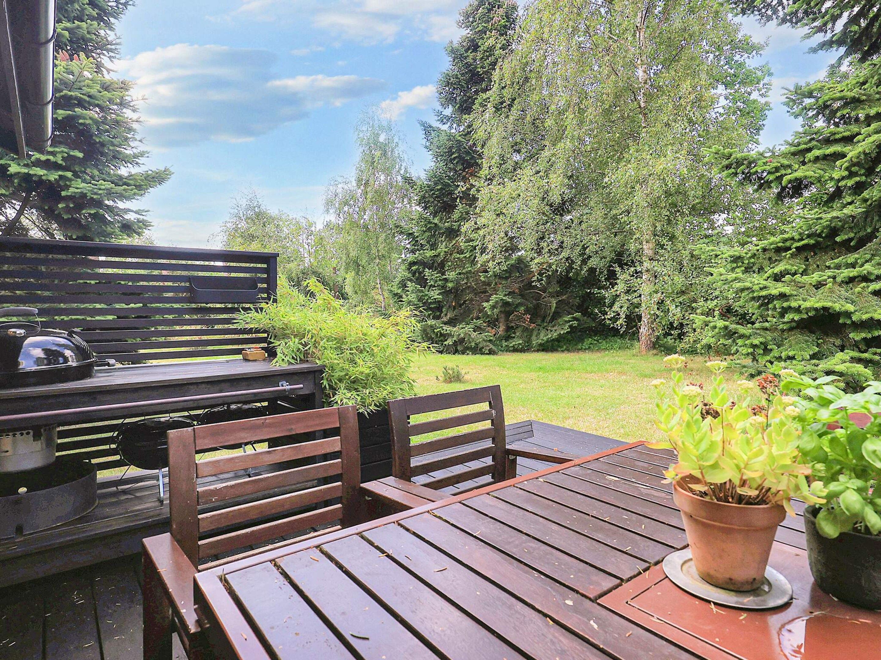 An outdoor patio with a wooden table and chairs, a grill, and potted plants.