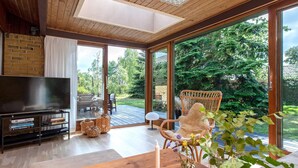 Una sala de estar moderna con televisor, muebles de madera y ventanas amplias que dan a un jardín.