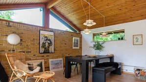Una habitación con pared de ladrillo, techo de madera, una mesa de comedor, sillas y una lámpara colgante.
