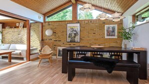 Un interior moderno con techo de madera, paredes de ladrillo, un área de comedor con banco y un sofá.