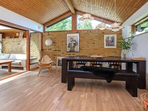 A modern interior with a wooden ceiling, brick walls, a dining area with a bench, and a sofa.