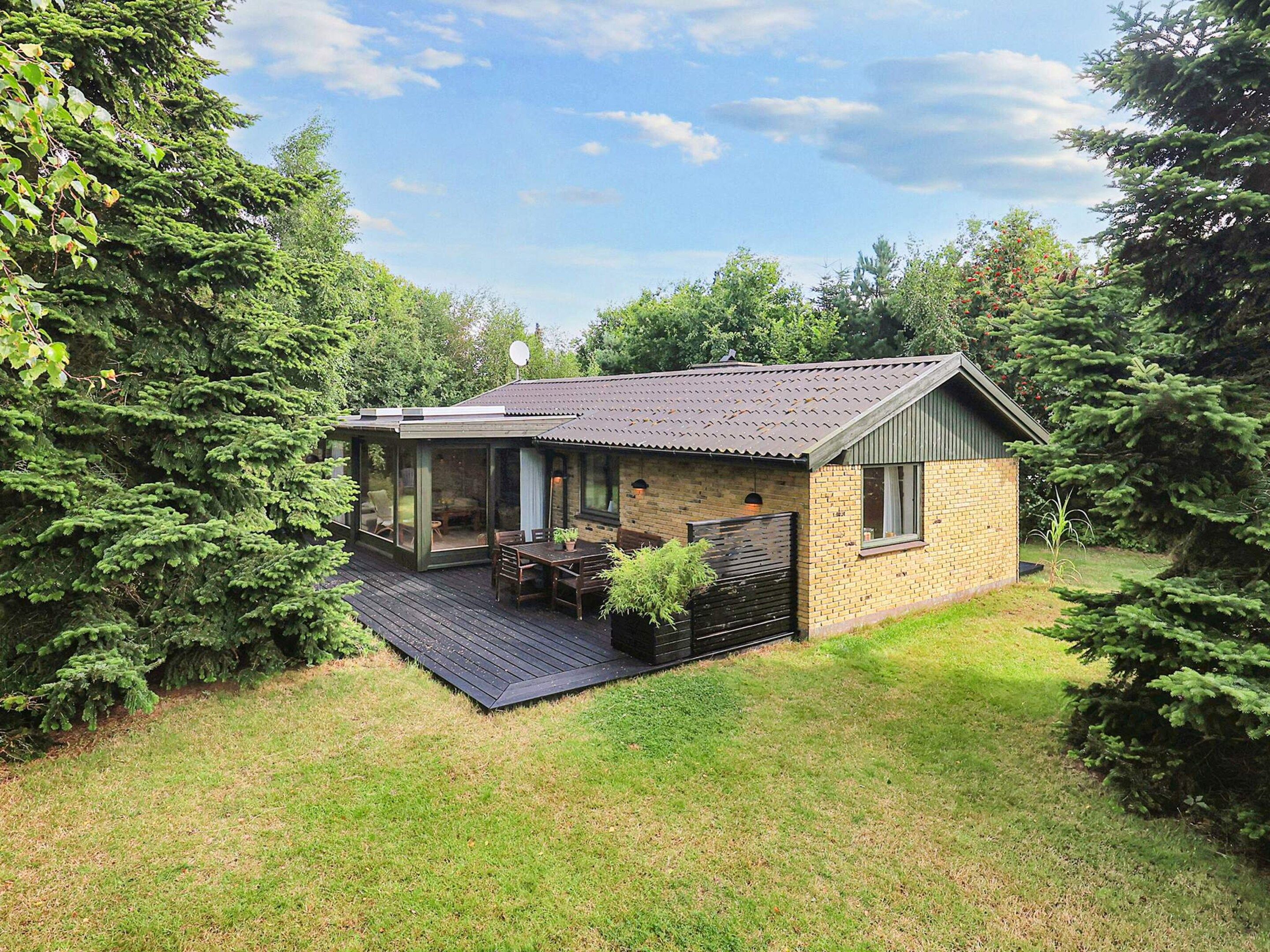 Une petite maison avec une terrasse, entourée d’arbres.