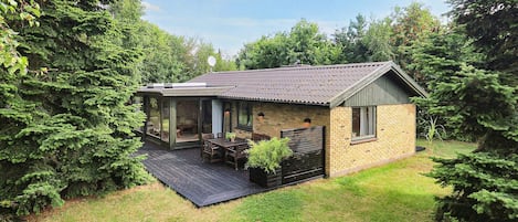 A small house with a deck, surrounded by trees.
