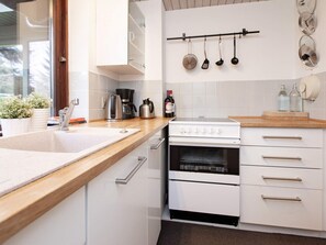 A modern kitchen with white cabinetry, a stainless steel sink, a coffee maker, a kettle, and a stove.