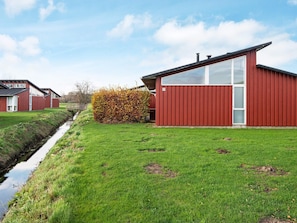 A modern red building with a glass facade, a grassy lawn, and a narrow water channel. - 5 Star Holiday Home in Bogense (Bogense)