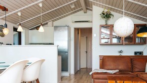 A modern kitchen with a central island, white chairs, a brown sofa, and pendant lighting. - 4 Star Holiday Home in Romo (Rømø)
