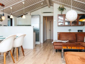 A modern kitchen with a central island, a dining area with white chairs, and a living space with a brown sofa.
