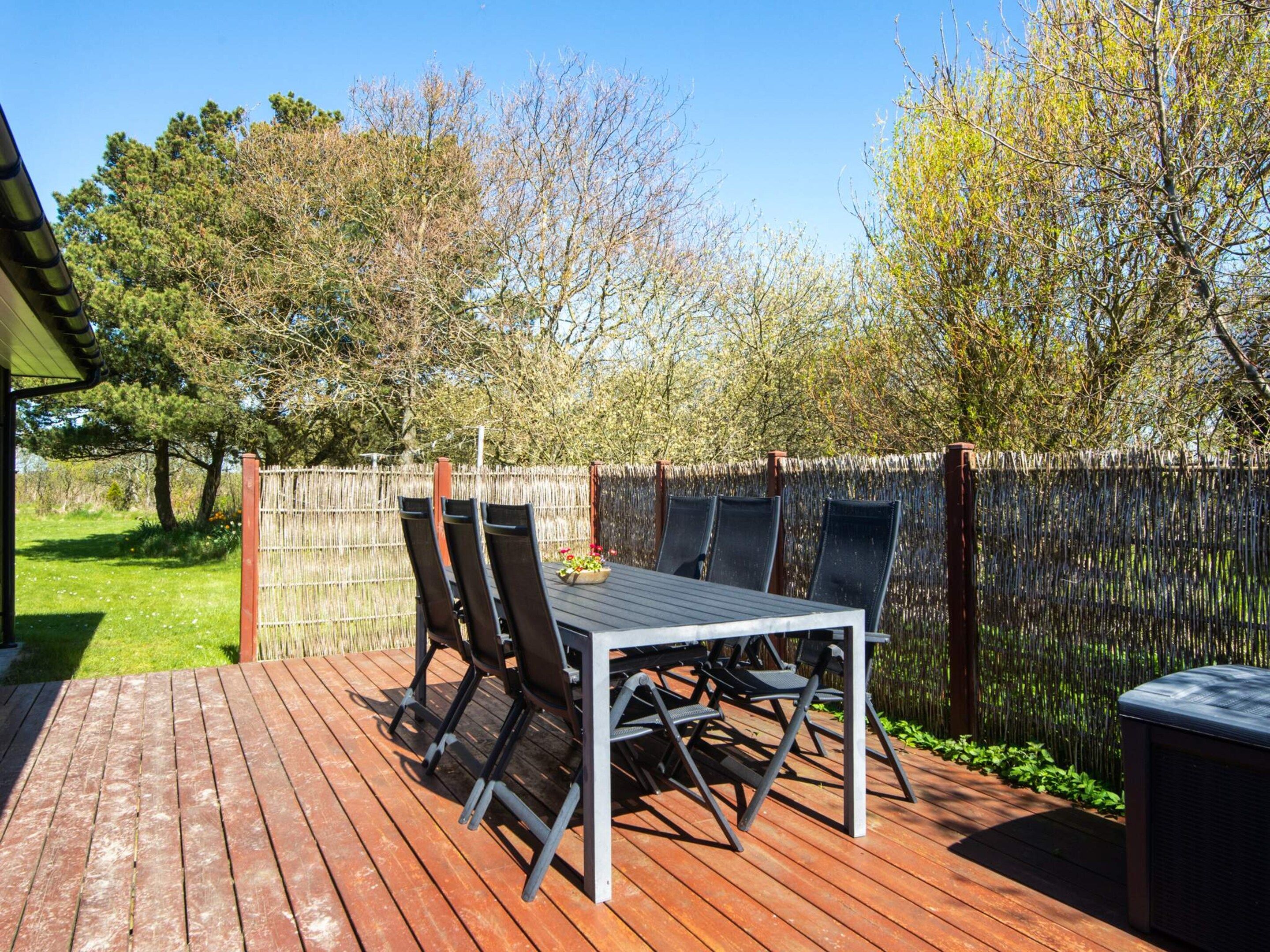 Une terrasse extérieure avec une table et des chaises, entourée d’une plateforme en bois et d’une clôture en bambou.