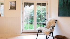A room with a large glass door leading to a garden, a white chair with a fluffy cushion, and a framed picture on the wall. - 5 Star Holiday Home in Laeso (Læsø)