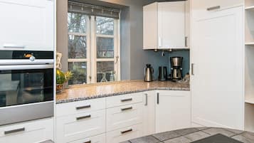 A modern kitchen with white cabinetry, a built-in oven, a window with a view, and a countertop with a coffee maker.