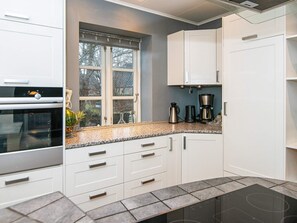 A modern kitchen with white cabinetry, a built-in oven, a window with a view, and a countertop with a coffee maker. - 4 Star Holiday Home in Broager (Broager)