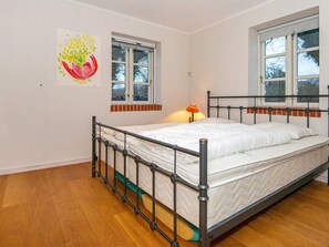A single bed with a metal frame in a room with wooden flooring, two windows, and a wall-mounted lamp. - 4 Star Holiday Home in Broager (Broager)