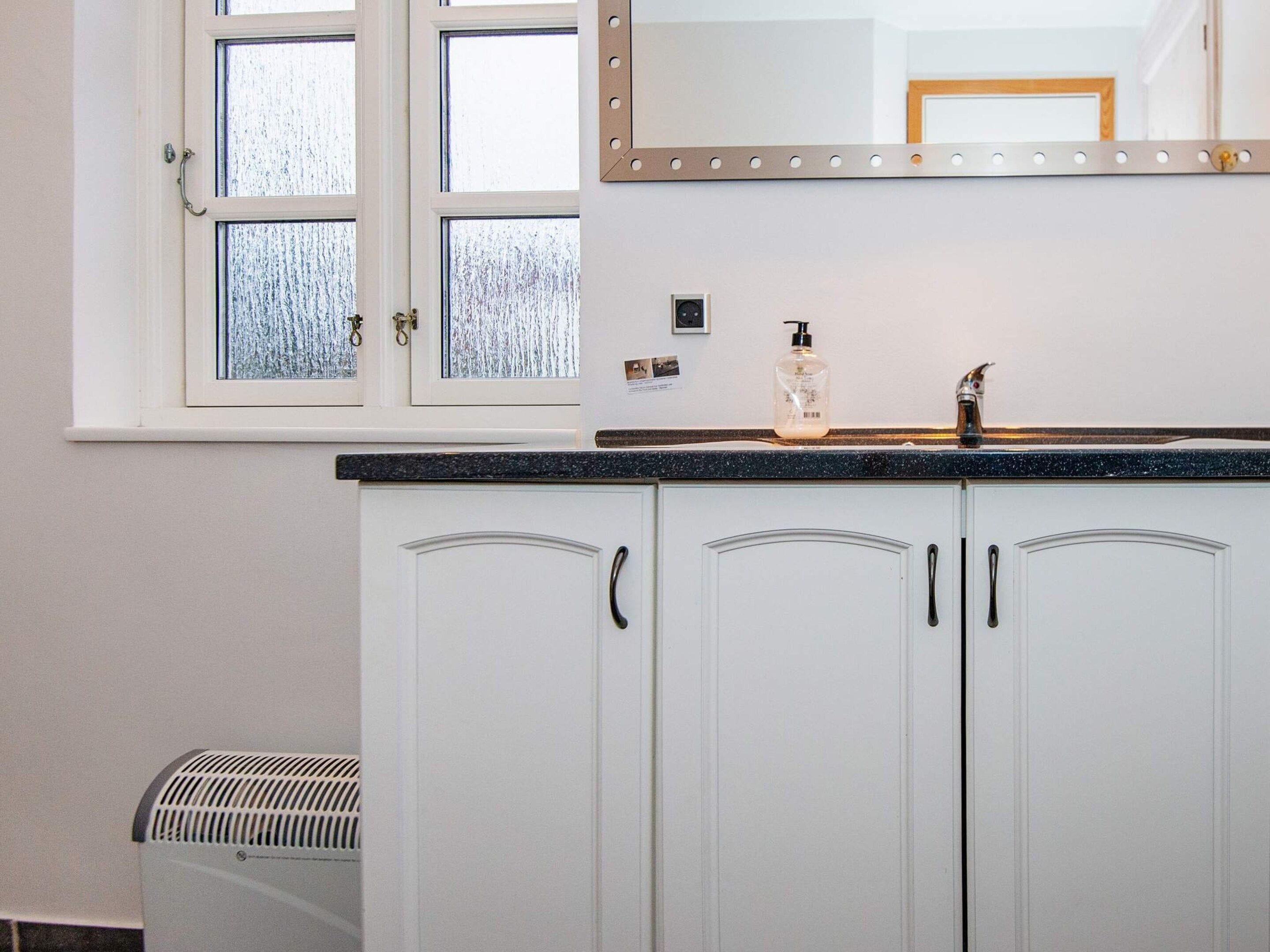 A bathroom with white cabinets, a sink with a soap dispenser, and a mirror above the mirror.