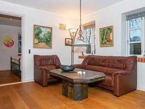 A room with a brown leather sofa, a table with a bowl and candles, and paintings on the walls. - 6 Person Holiday Home in Broager (Broager)