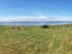 A grassy area with a picnic table and benches, a body of water in the background, and a clear sky. - 6 Person Holiday Home in Broager (Broager)