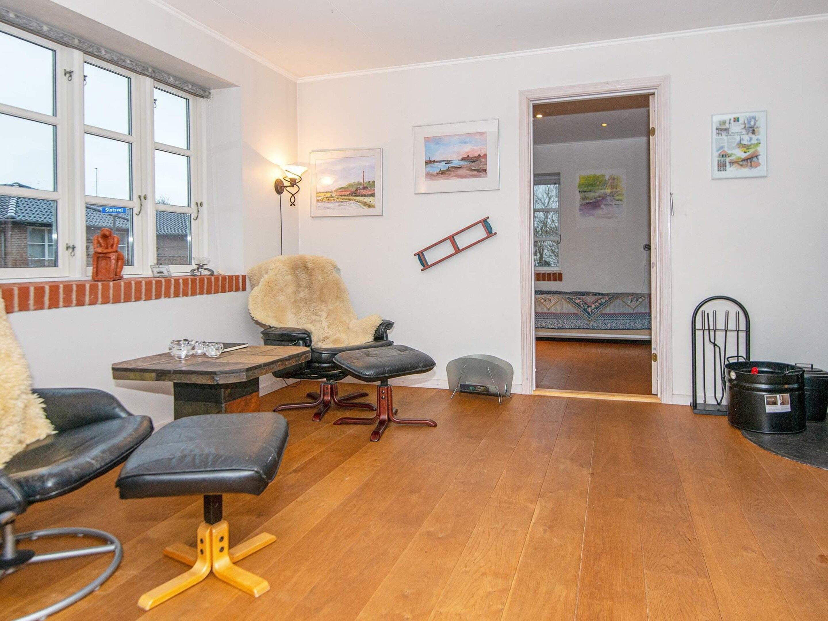 A room with a wooden floor, a black leather chair, a wooden table, and a window with a view of a building.