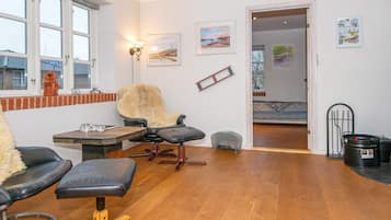 A room with a wooden floor, a black leather chair, a wooden table, and a window with a view of a building.