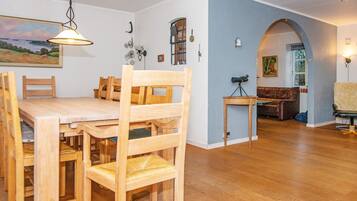 A dining area with a wooden table and chairs, a hanging light fixture, and a painting on the wall.