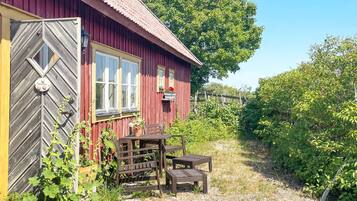 A red wooden building with a door, windows, and a small outdoor seating area with a table and chairs.