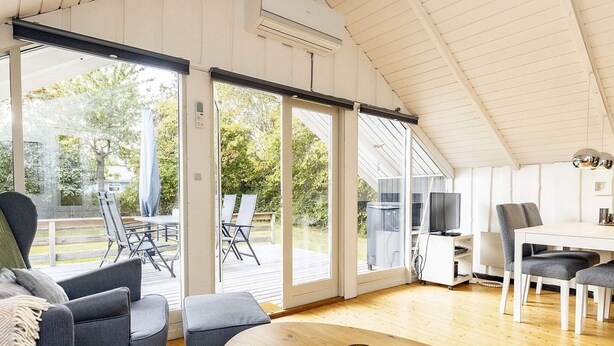 A spacious living area with a large wooden table, grey upholstered seating, and a view of the outdoors through large sliding glass doors. - 6 Person Holiday Home in Tranekaer (Tranekaer)