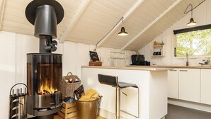 A modern kitchen with a wood-burning stove, white cabinets, and a window overlooking greenery. - 6 Person Holiday Home in Tranekaer (Tranekaer)