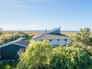 A house with a sloped roof, surrounded by trees and a view of the sea.