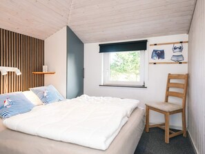 A bedroom with a bed, a chair, a window, and a wall with a shelf and pictures. - 5 Star Holiday Home in Ebeltoft (Ebeltoft)
