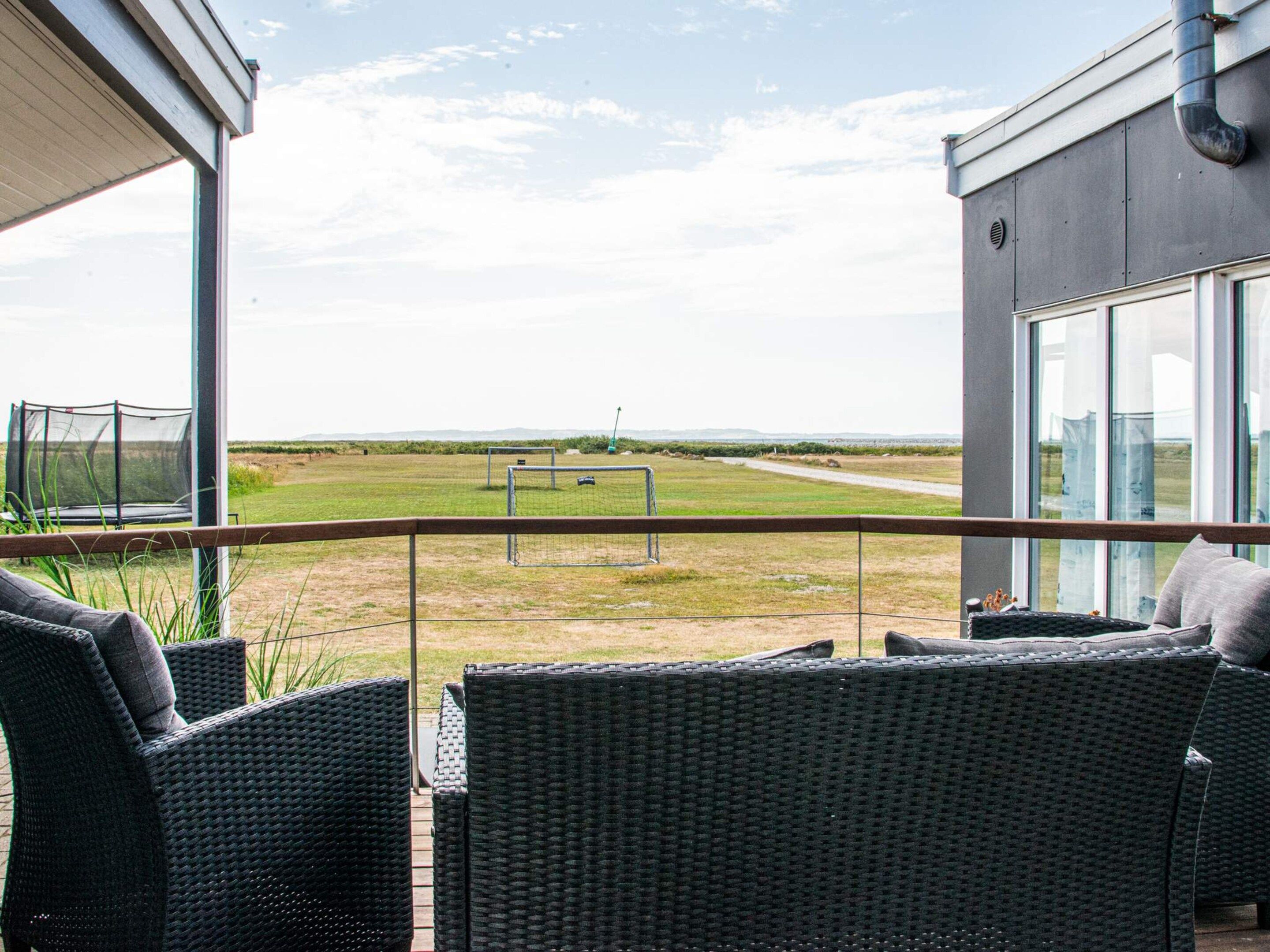 Een balkon met rieten meubilair, uitzicht op een sportveld en een gebouw met grote ramen.