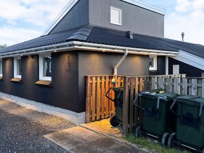 A modern two-story house with a dark facade, a sloped roof, and a wooden fence.
