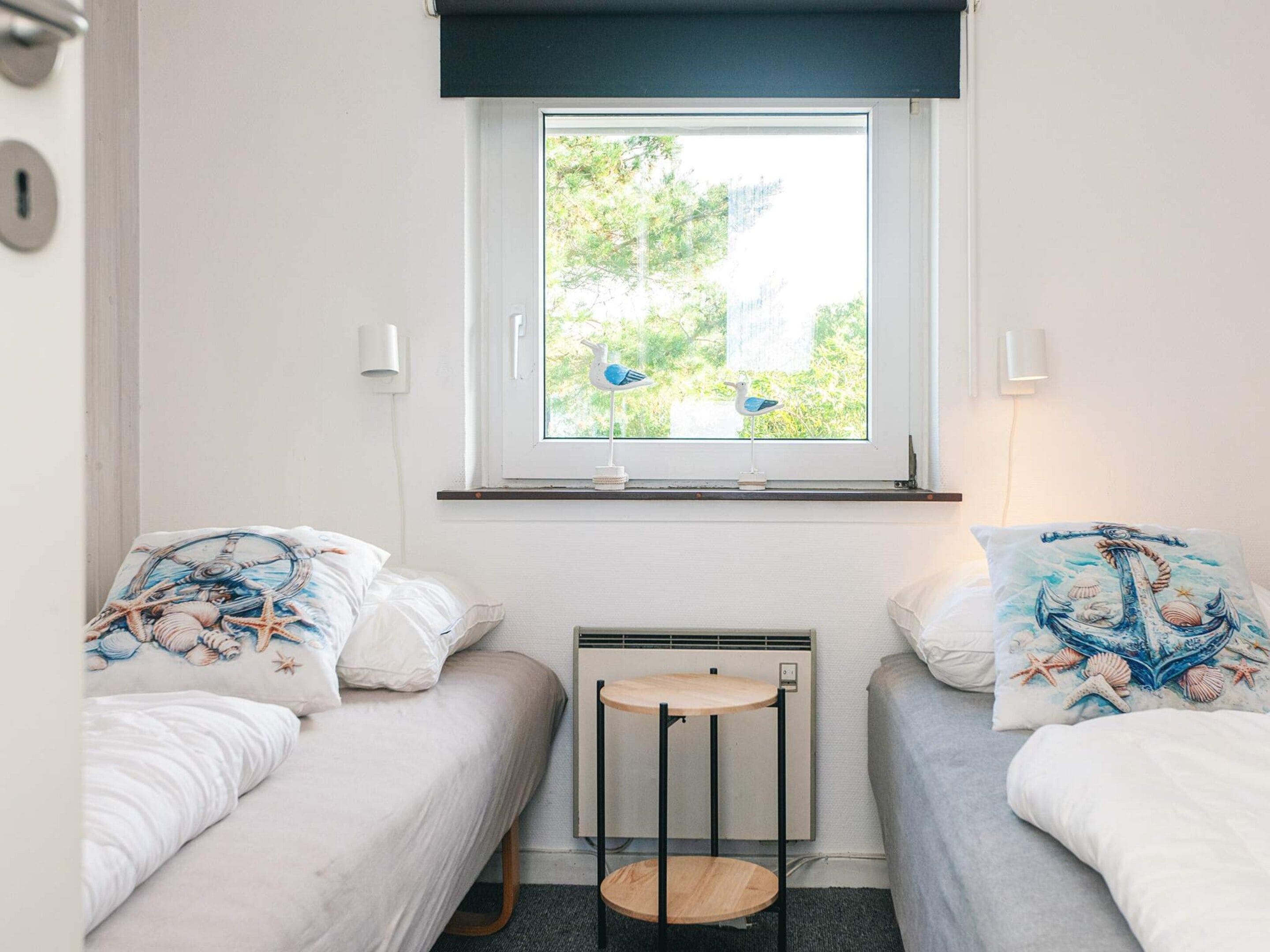 Et værelse med to senge, et lille bord, et vindue med udsigt til grønne områder og en fastgjort varmeovn.