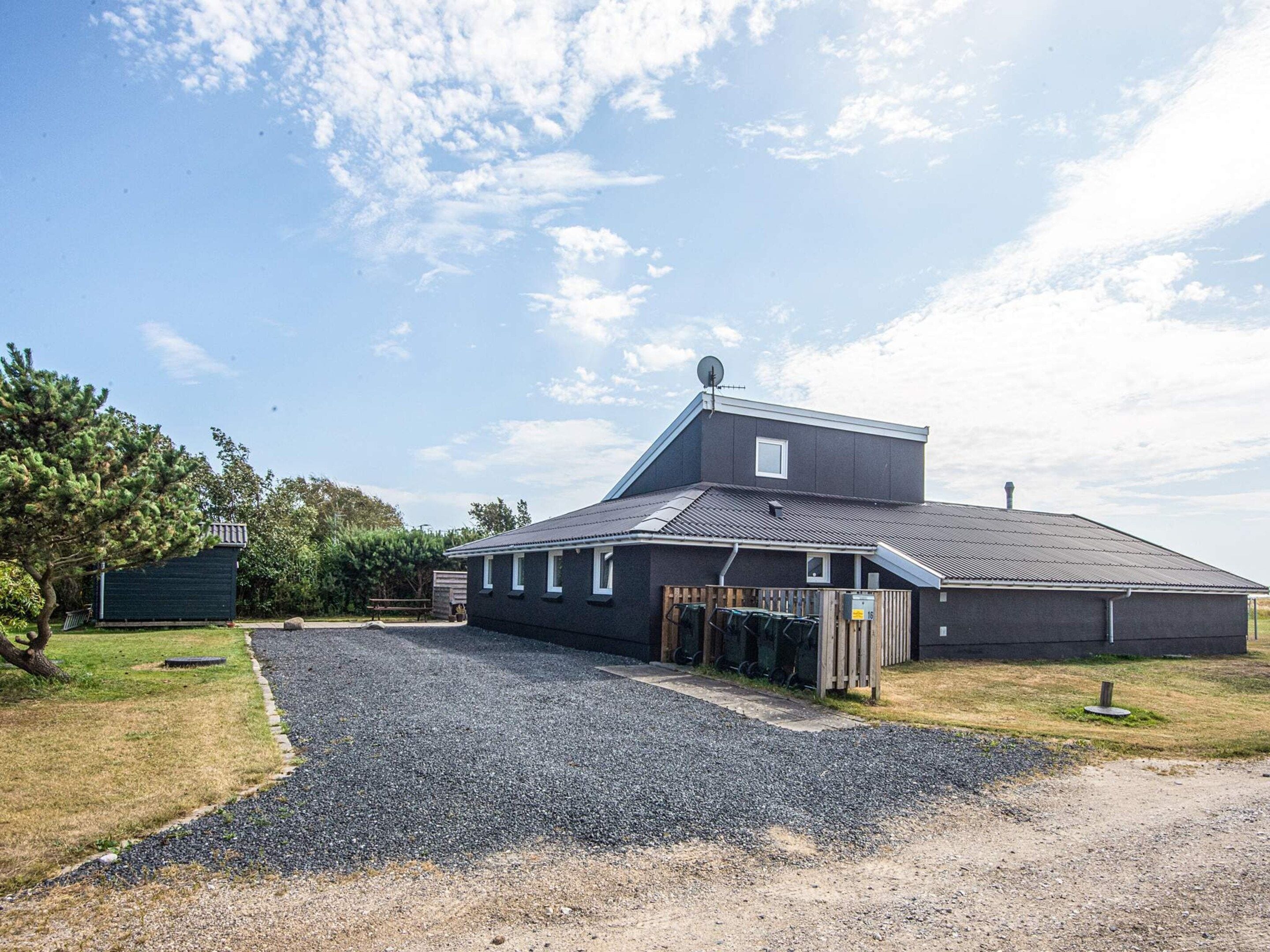 A two-story building with a sloped roof, a fenced driveway, and a gravel path leading to the entrance.
