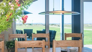 A dining area with wooden chairs and tables, large windows, and a view of a grassy field. - 5 Star Holiday Home in Ebeltoft (Ebeltoft)