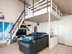 A modern living space with a black leather sofa, a wooden staircase, and a flat-screen TV. - 5 Star Holiday Home in Ebeltoft (Ebeltoft)
