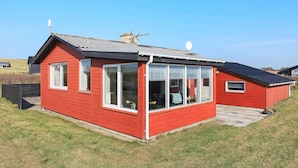 Punainen, yhden kerroksen talo, jossa on suuret ikkunat ja kalteva katto.